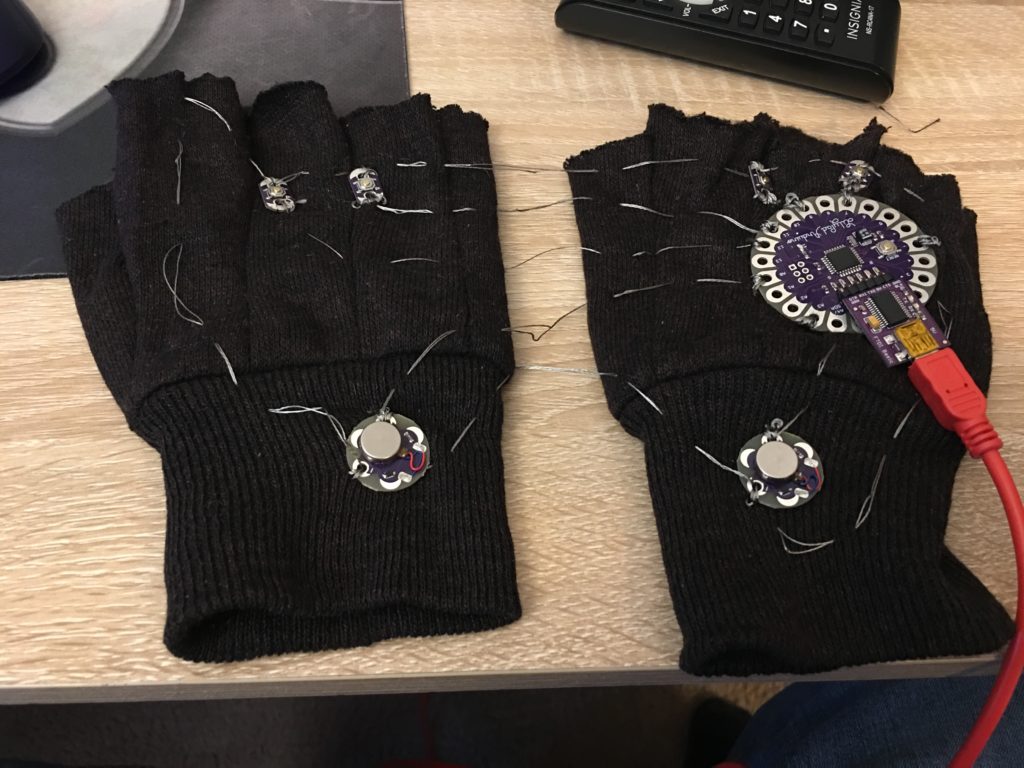Holding Hands: A pair of gloves connected by conductive threads to be worn by two people. Pressing the buttons on the gloves triggers a vibration in the motor of the glove, allowing for the wearers to communicate nonverbally.