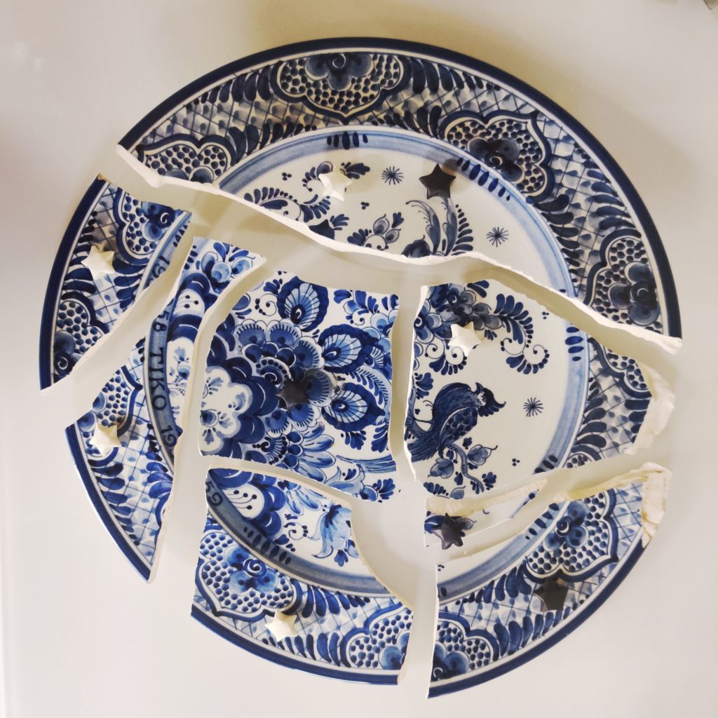Shattered Blue and white porcelain plate with white and black paper stars placed around it.