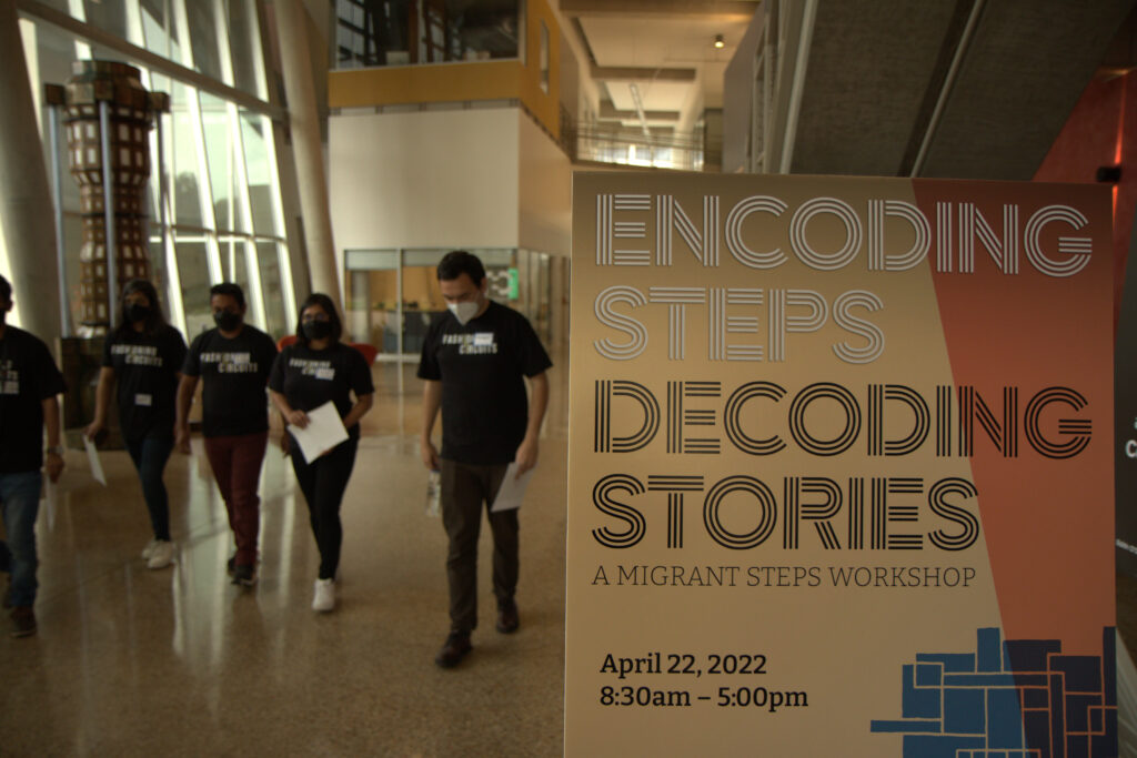 The Encoding Steps: Decoding Stories Poster in the foreground with participants of the workshop walking in the background.