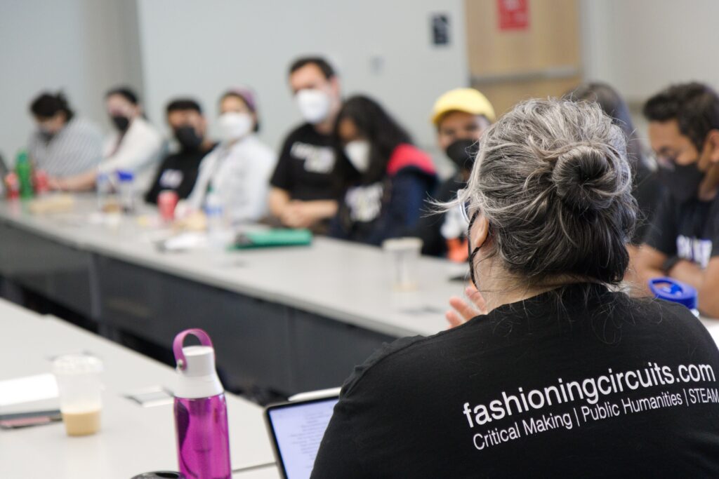 Dr. Knight in the foreground with a Fashioning Circuits Logo highlighted and members of the Migrant Steps Team in the background.